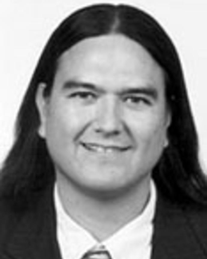 Donald Warne has long straight black hair. He is wearing a suit.