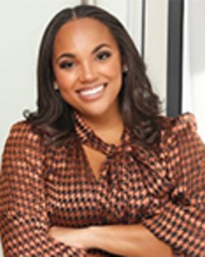Zerita Buchanan has medium-length black hair. She is wearing a printed brown blouse and smiling with her arms crossed.