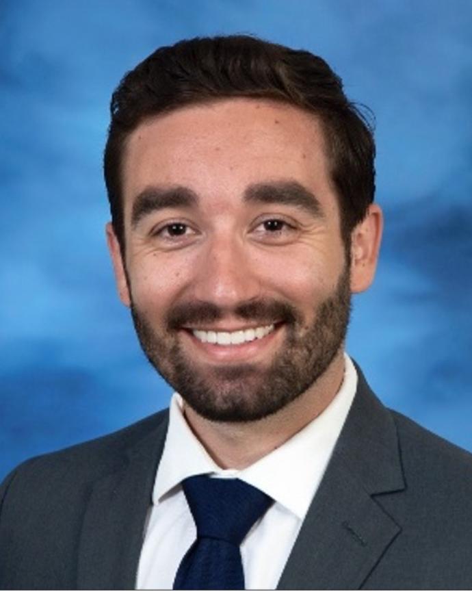Michael Harding has short black hair and facial hair. He is wearing a suit.