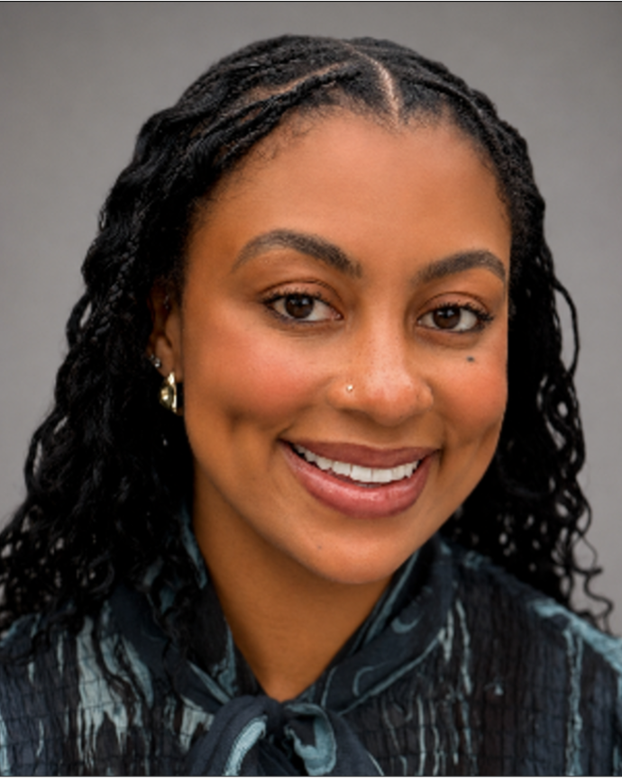 Tiana Walker has long micro-braids. She is wearing a dark green velvet blouse.