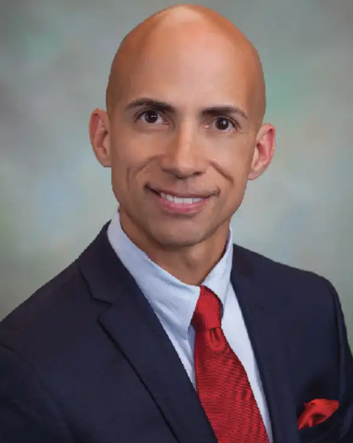 Jose Santana is wearing a black blazer, white shirt, and red tie and hankerchief. He is bald.